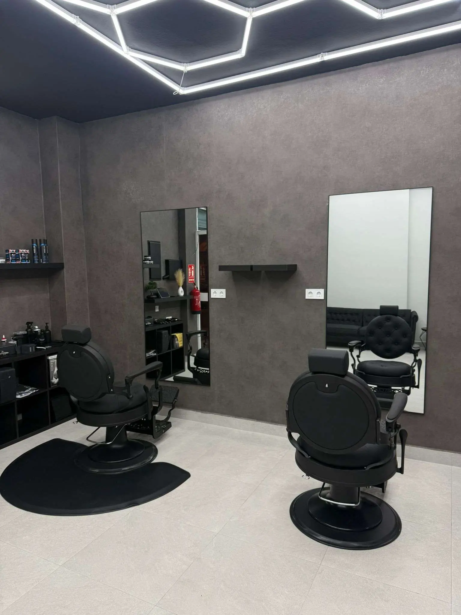 Interior moderno de barbería con sillón de barbero, lavacabezas y luces hexagonales en Ayamonte